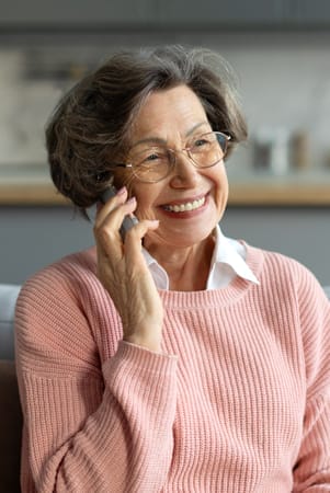 Happy senior woman in a pink sweater having a pleasant conversation, sitting on her couch at home.